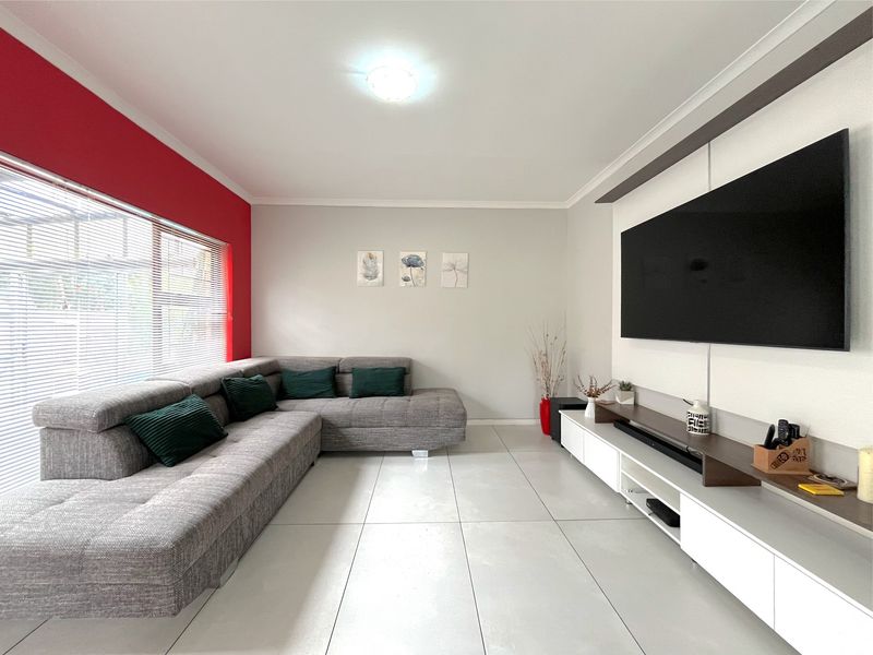 A bright and modern living room featuring large format floor tiles, a feature wall, and integrated window blinds.