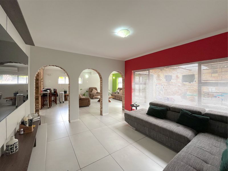 Spacious open-plan living area featuring distinctive brick archways, large windows with blinds, and neutral tiled flooring, creating a bright and connected living space.