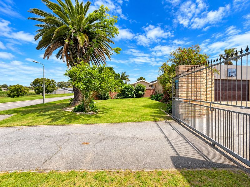 Front exterior view featuring a metal sliding gate, brick pillar, asphalt driveway, and established garden with a large palm tree.