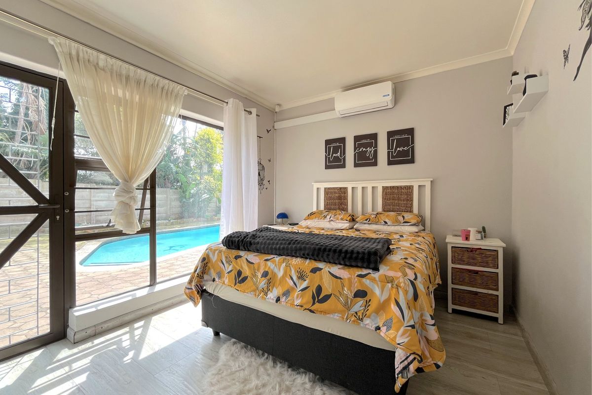 A bright bedroom featuring laminate flooring, a split-system air conditioner, and a large sliding glass door providing direct access to the pool area.