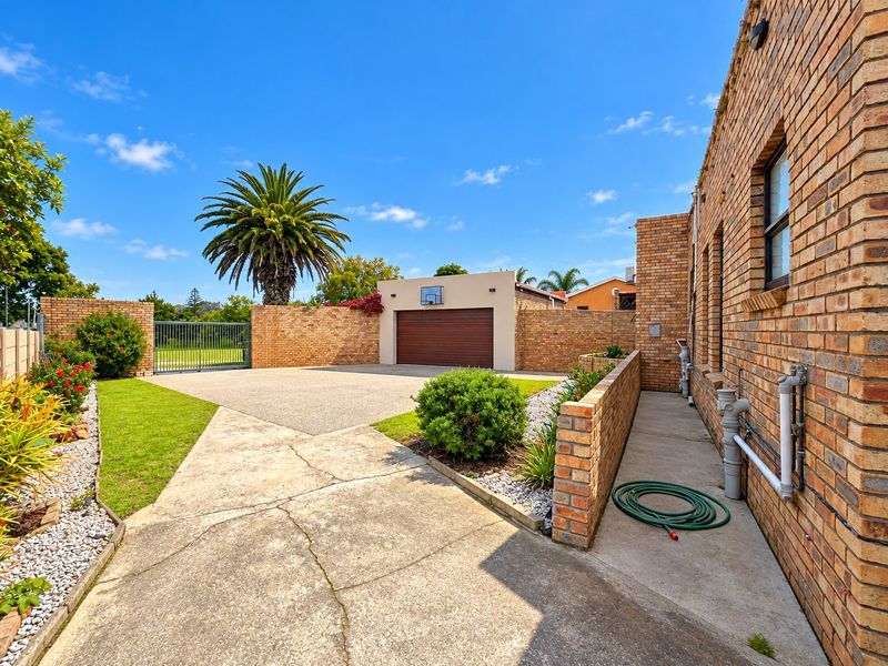 A well-maintained rear exterior featuring a brick facade, concrete driveway, single garage, and landscaped garden areas with a secure perimeter wall.