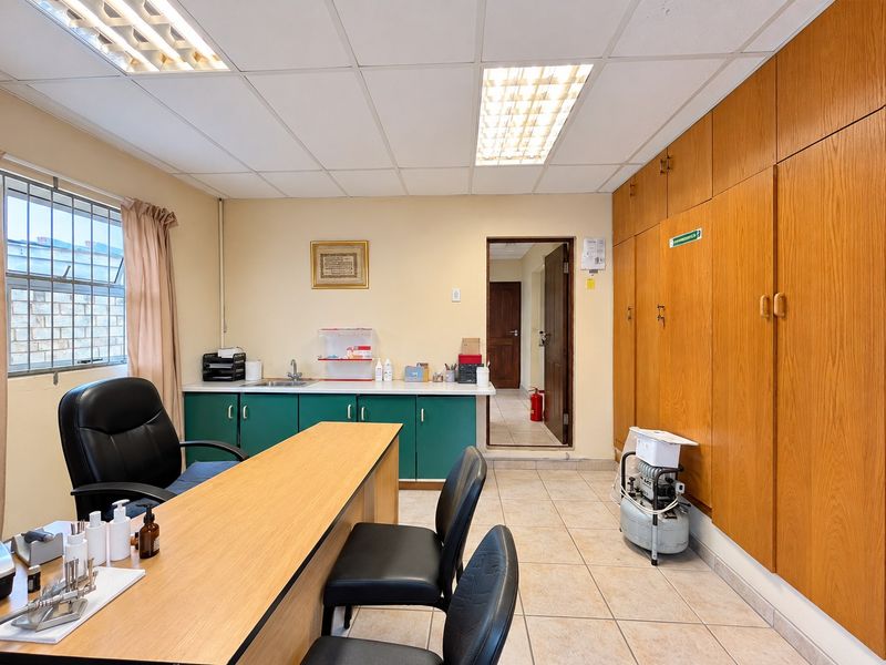 A functional office space featuring built-in wooden cabinetry, tiled flooring, a drop ceiling with integrated lighting, and a small built-in sink area.