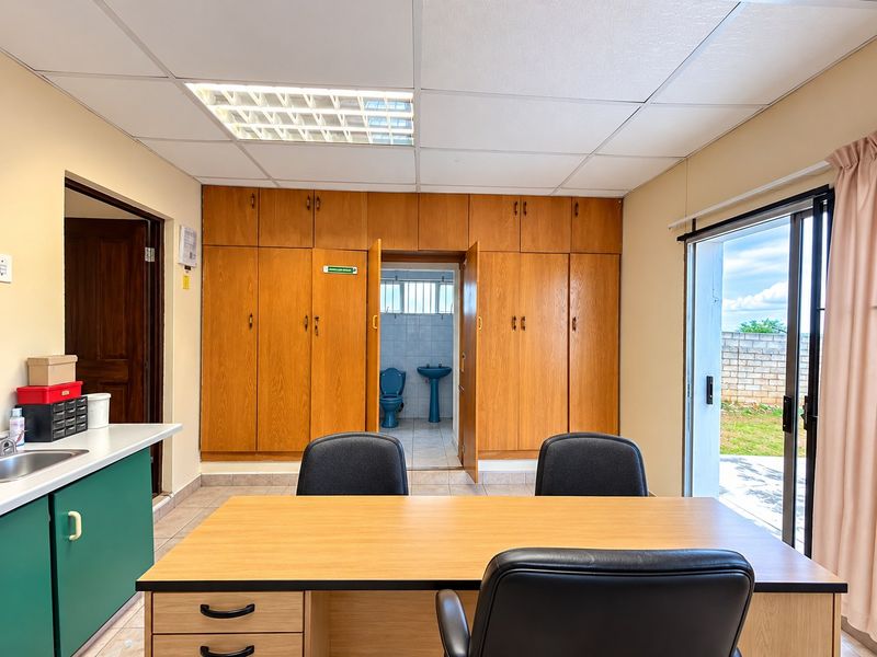 A functional office space featuring extensive built-in wooden cabinetry, a drop ceiling with recessed lighting, and direct access to an outdoor area.