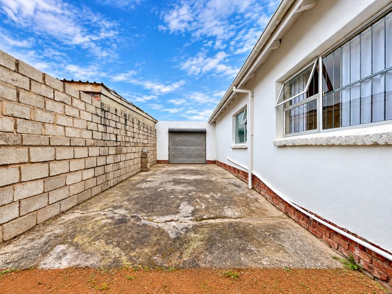 Rear exterior area featuring a concrete driveway, a roller shutter garage door, and a cinder block boundary wall.
