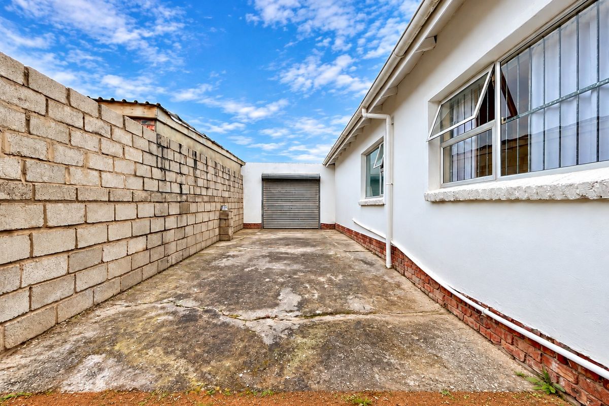 Rear exterior area featuring a concrete driveway, a roller shutter garage door, and a cinder block boundary wall.