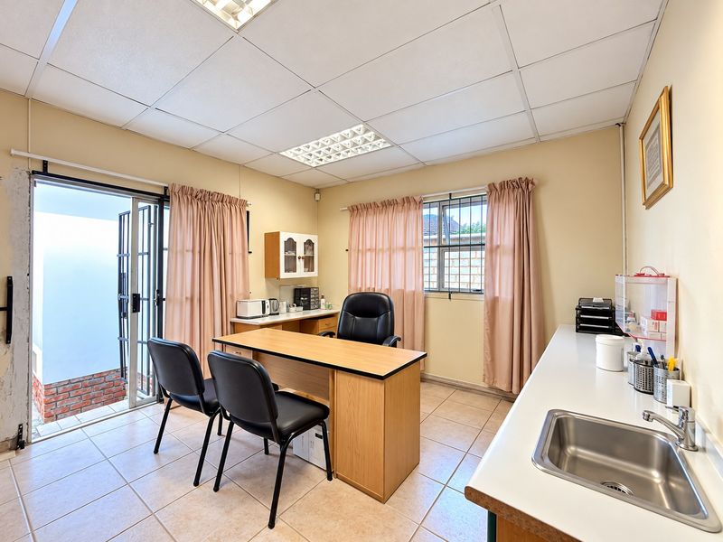 Functional office space featuring tiled flooring, a built-in sink with laminate countertop, drop ceiling, and direct access to an outdoor area via sliding doors.