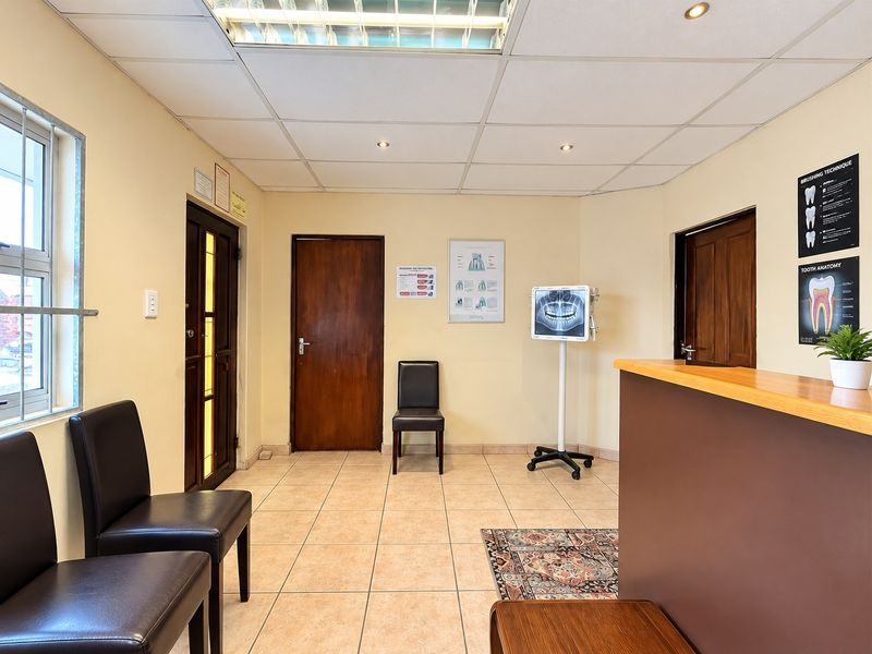A functional reception or waiting area featuring tiled flooring, a suspended ceiling with recessed lighting, and wooden door finishes.