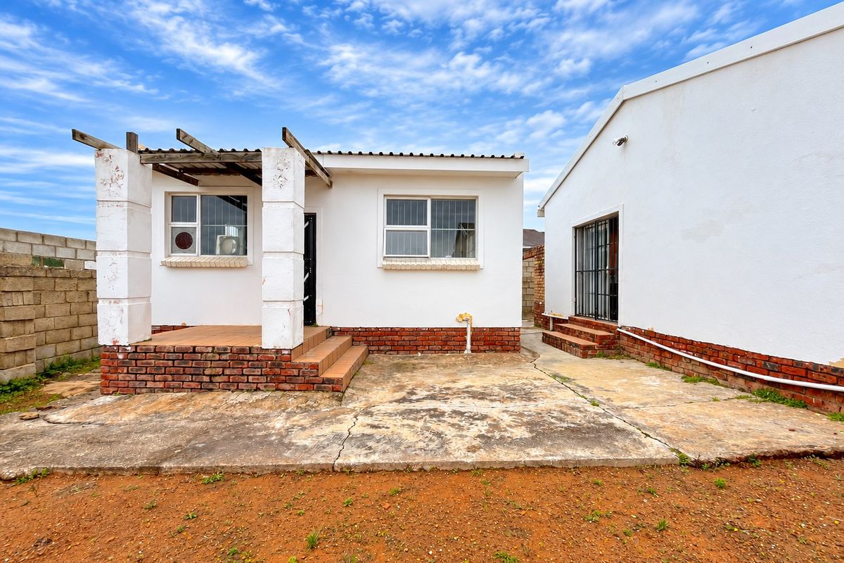 Rear exterior view of the property featuring a concrete patio area, brick base detailing, and a small pergola structure.