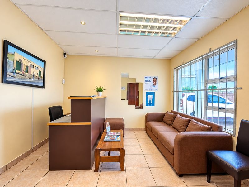 A functional reception or waiting area featuring ceramic floor tiles, a suspended ceiling with integrated lighting, and large windows fitted with security bars.