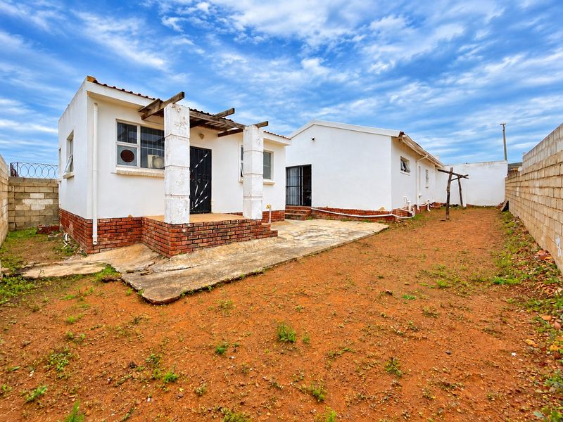 Rear view of the property featuring a concrete patio, pergola structure, and a large, unlandscaped yard enclosed by perimeter walls.