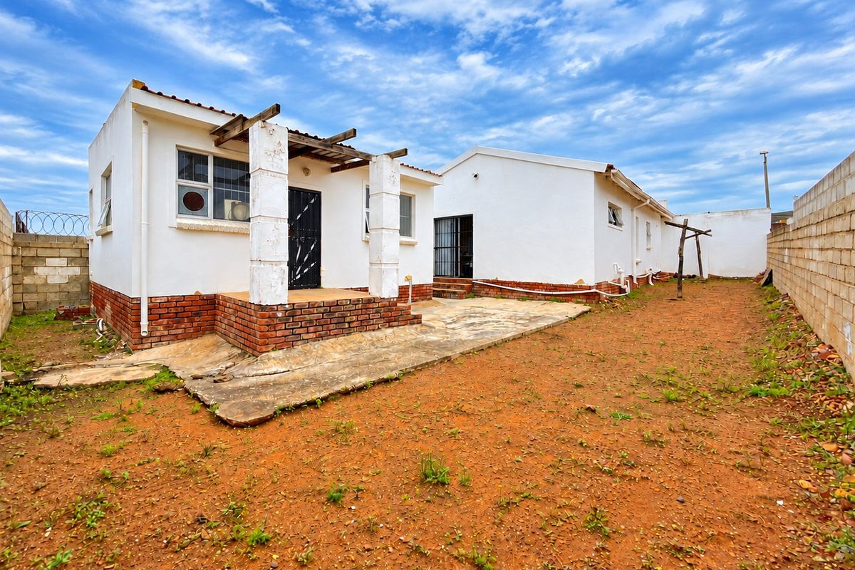 Rear view of the property featuring a concrete patio, pergola structure, and a large, unlandscaped yard enclosed by perimeter walls.