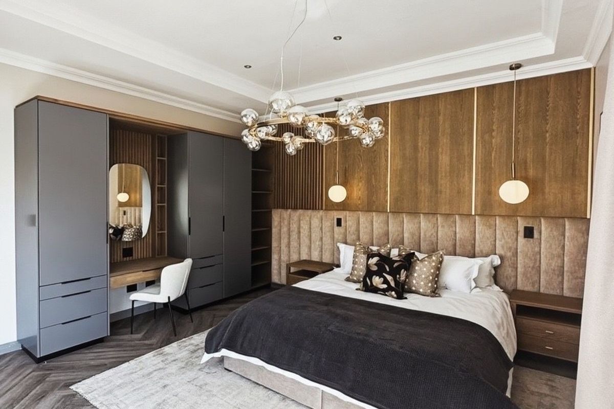 Luxurious bedroom featuring custom built-in wardrobes, integrated vanity, upholstered headboard, and elegant herringbone flooring with sophisticated recessed lighting.