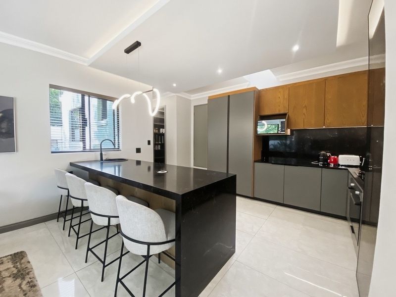 Modern kitchen featuring a large central island with stone countertops, sleek two-tone cabinetry, integrated appliances, and high-quality tiled flooring.