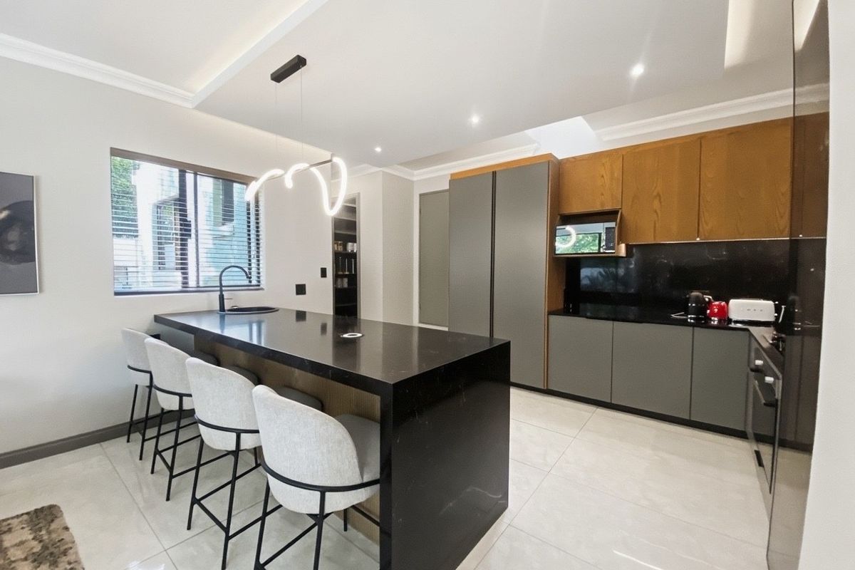 Modern kitchen featuring a large central island with stone countertops, sleek two-tone cabinetry, integrated appliances, and high-quality tiled flooring.
