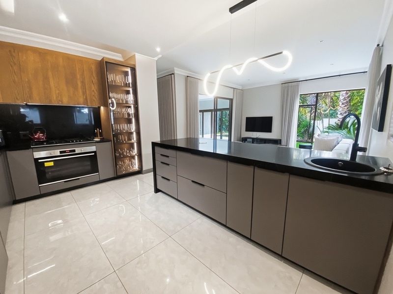 Modern open-plan kitchen featuring a large island with dark stone countertops, integrated appliances, sleek cabinetry, and high-end finishes overlooking the living area.