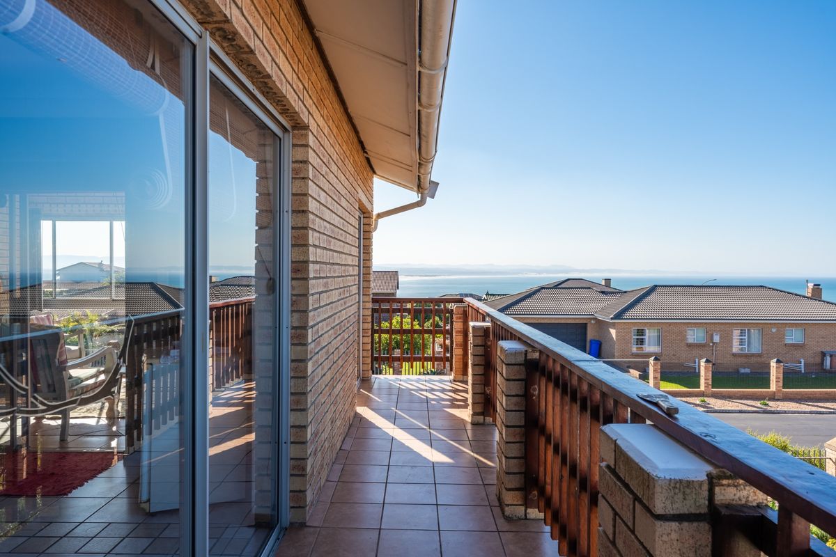 A spacious balcony featuring tiled flooring, a timber balustrade, and brick exterior walls, offering elevated views of the surrounding neighborhood and coastline.