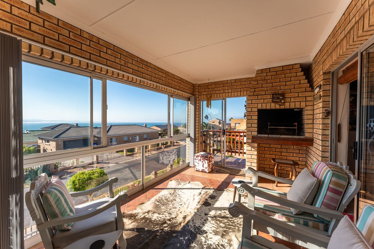 Enclosed balcony featuring a built-in brick braai, tiled flooring, and expansive glass windows offering scenic coastal and neighbourhood views.