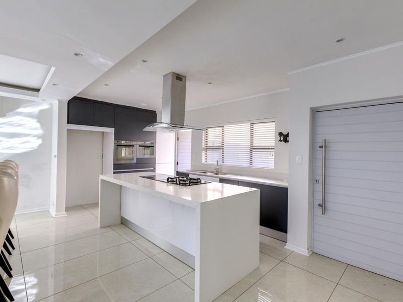 Modern kitchen featuring a central island with gas hob, sleek cabinetry, built-in ovens, and large format floor tiles.