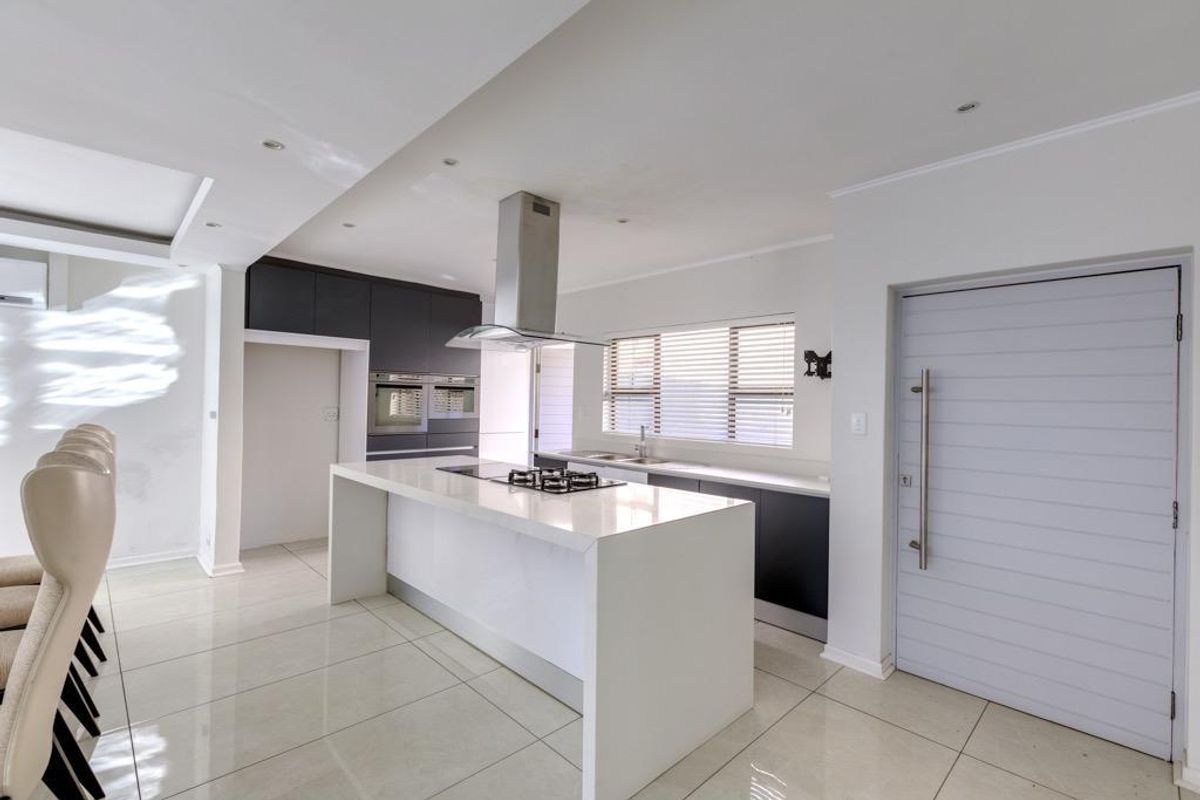 Modern kitchen featuring a central island with gas hob, sleek cabinetry, built-in ovens, and large format floor tiles.