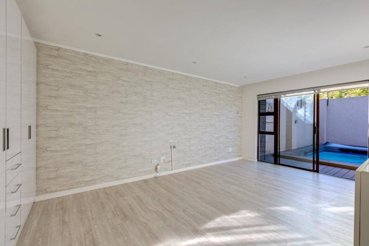 A bright, empty bedroom featuring built-in cupboards, textured wallpaper, and sliding glass doors that open directly onto a private patio with a pool.