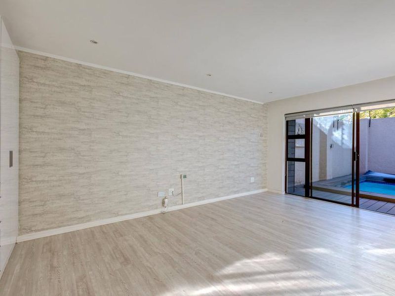 A bright, empty bedroom featuring built-in cupboards, textured wallpaper, and sliding glass doors that open directly onto a private patio with a pool.