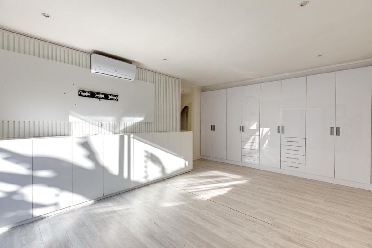 A bright, modern living room featuring extensive built-in white cabinetry, slatted wall detailing, and a wall-mounted air conditioning unit with light wood-look flooring.