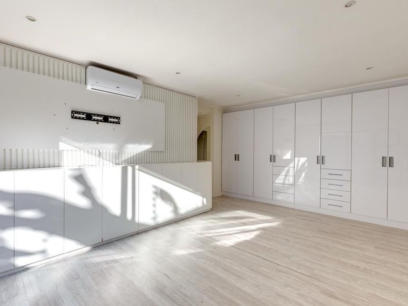A bright, modern living room featuring extensive built-in white cabinetry, slatted wall detailing, and a wall-mounted air conditioning unit with light wood-look flooring.