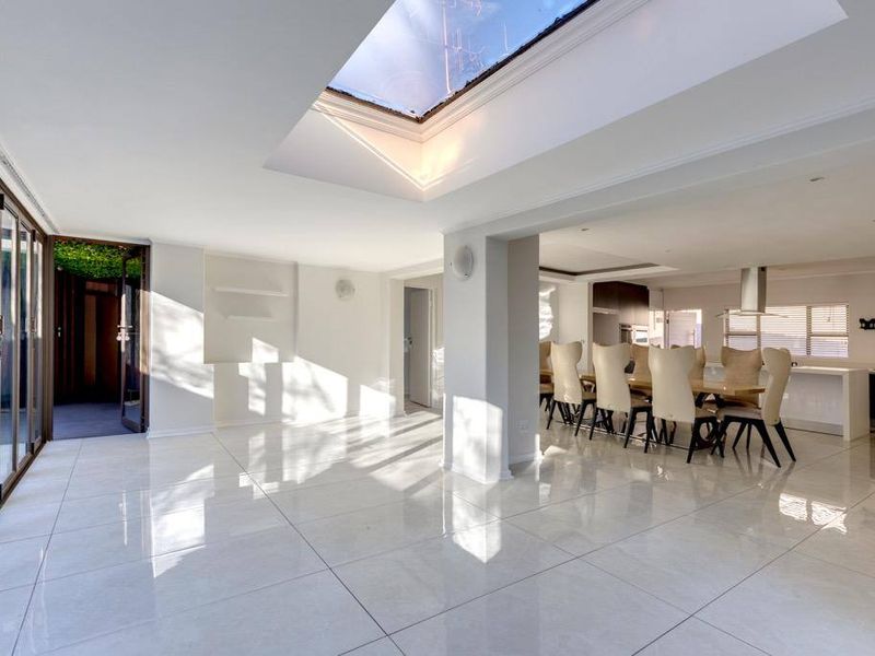 Spacious open-plan living and dining area featuring large format floor tiles, a prominent skylight, and seamless access to the outdoor patio through sliding doors.