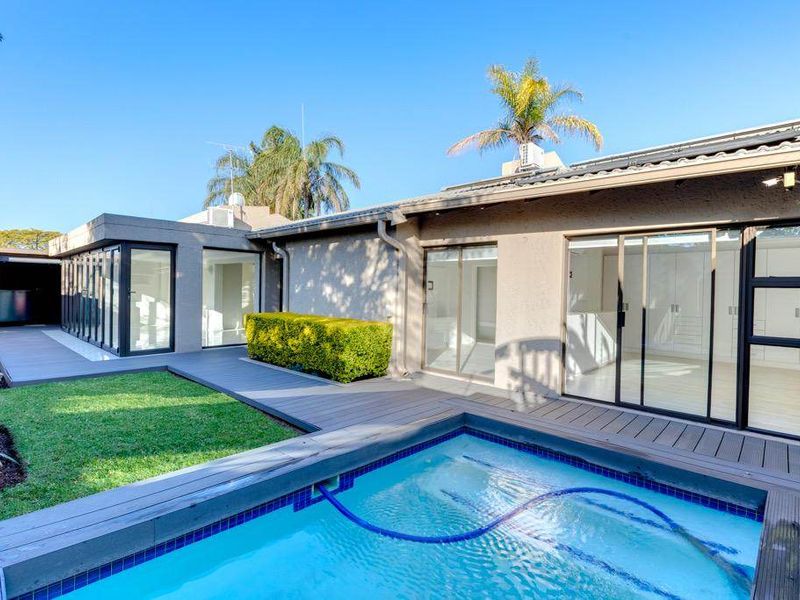 Rear exterior view featuring a modern swimming pool, composite decking, and seamless indoor-outdoor flow through large sliding and bi-fold glass doors.