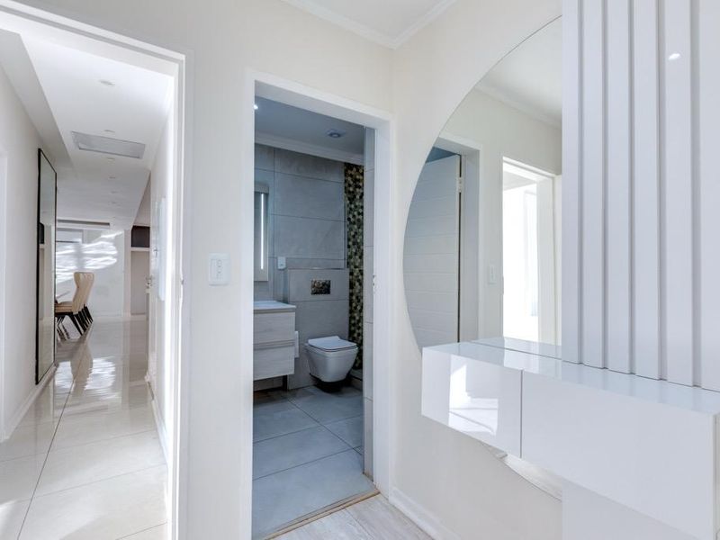 A bright, modern hallway featuring polished tiled flooring, recessed lighting, and a sleek built-in vanity console with a large mirror.