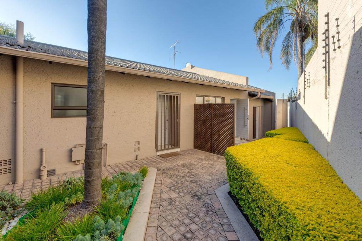 Rear exterior view featuring a paved walkway, privacy screen, and well-maintained garden hedge alongside the property boundary wall.