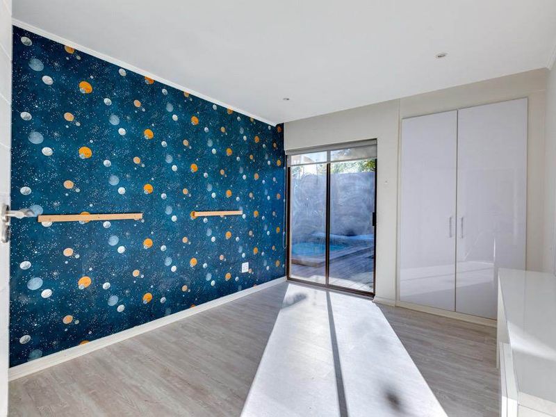 A bright, empty bedroom featuring built-in cupboards, laminate flooring, and a sliding glass door providing direct access to the outdoor pool area.