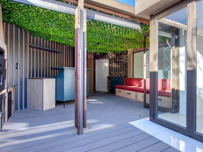 A modern covered patio featuring timber decking, built-in braai, and stylish slat wall cladding, seamlessly connecting to the interior through large glass sliding doors.