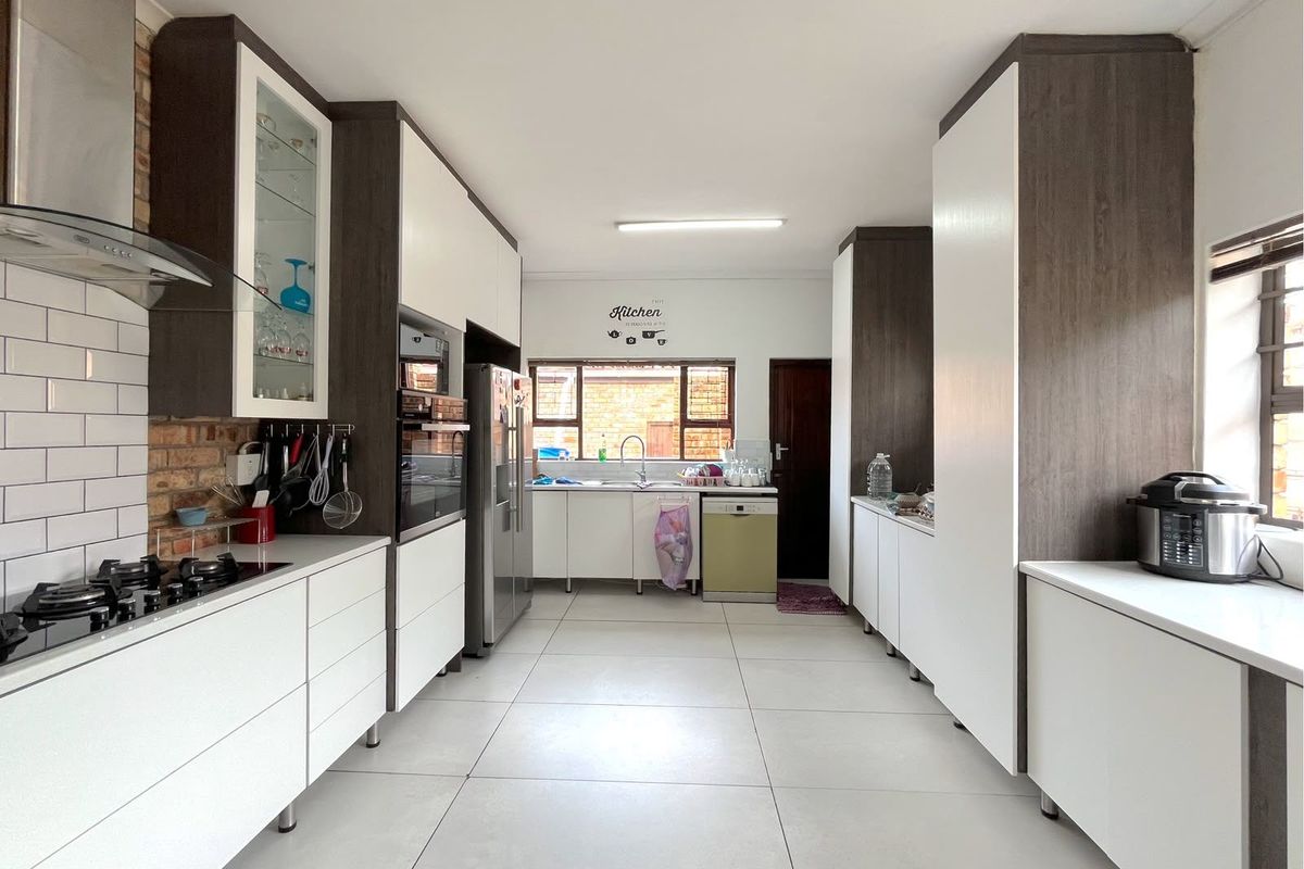 Modern galley-style kitchen featuring white cabinetry, exposed brick accents, gas hob, built-in oven, and large format floor tiles.
