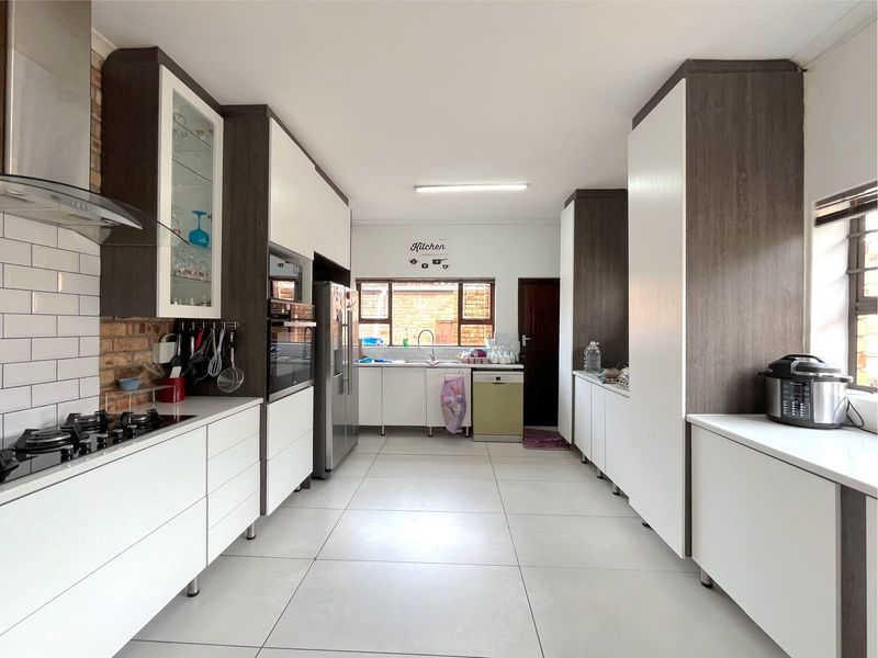 Modern galley-style kitchen featuring white cabinetry, exposed brick accents, gas hob, built-in oven, and large format floor tiles.