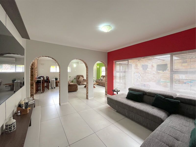 Spacious open-plan living area featuring distinctive brick archways, large windows with venetian blinds, and neutral tiled flooring throughout.