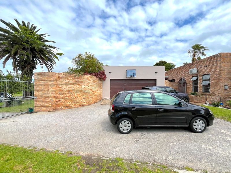 Front exterior view of the property featuring a brick boundary wall, metal gate, asphalt driveway, and garage access.