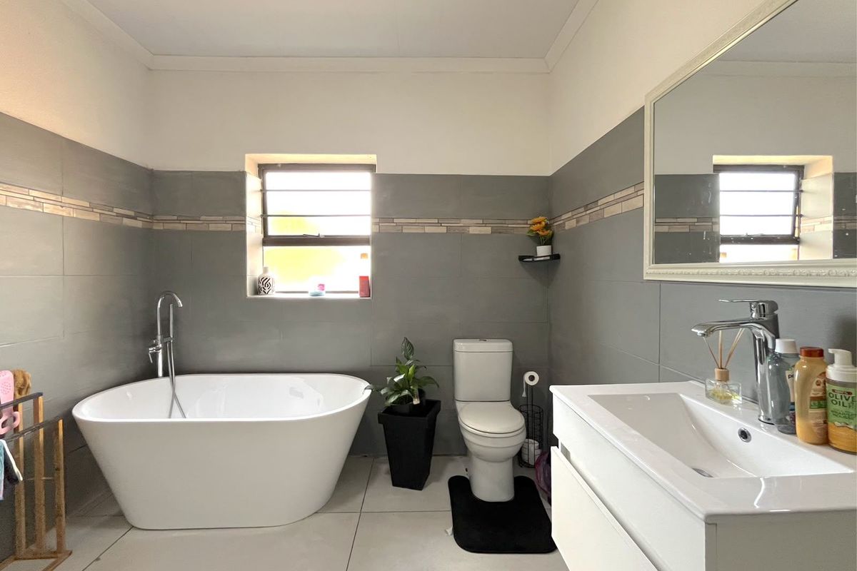 Modern bathroom featuring a sleek freestanding bathtub, wall-mounted vanity with basin, and neutral grey tiled walls with a decorative border.