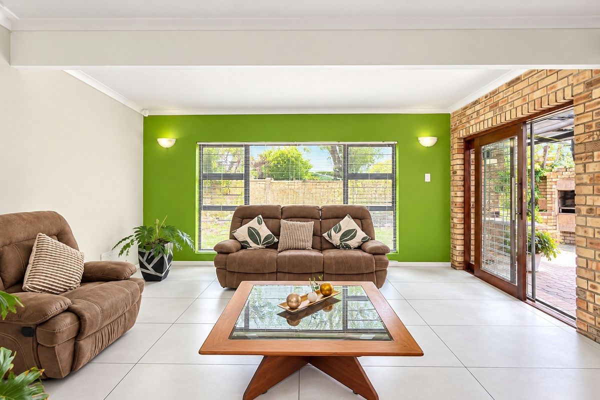 Spacious living room featuring large format floor tiles, an exposed brick wall, and sliding glass doors providing seamless access to the outdoor patio area.