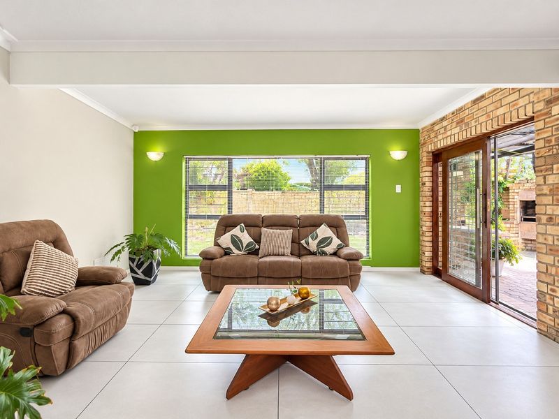 Spacious living room featuring large format floor tiles, an exposed brick wall, and sliding glass doors providing seamless access to the outdoor patio area.