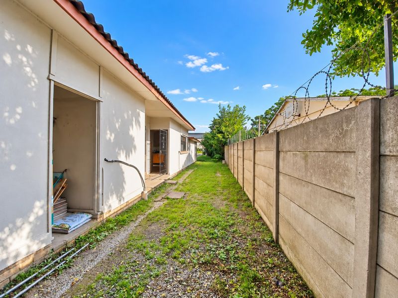 A side exterior view of the property featuring a precast concrete boundary wall with razor wire and an unpaved garden area.