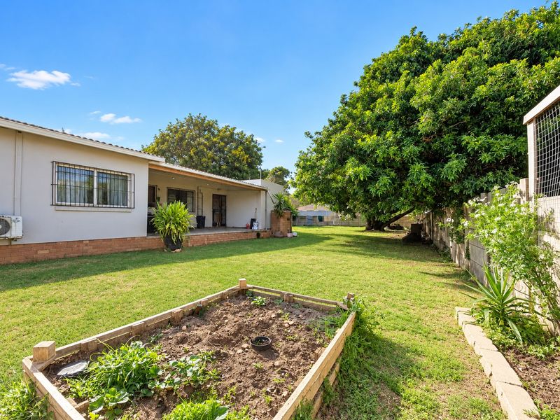 Spacious rear garden featuring a covered patio, established trees, a raised vegetable bed, and a secure boundary wall.