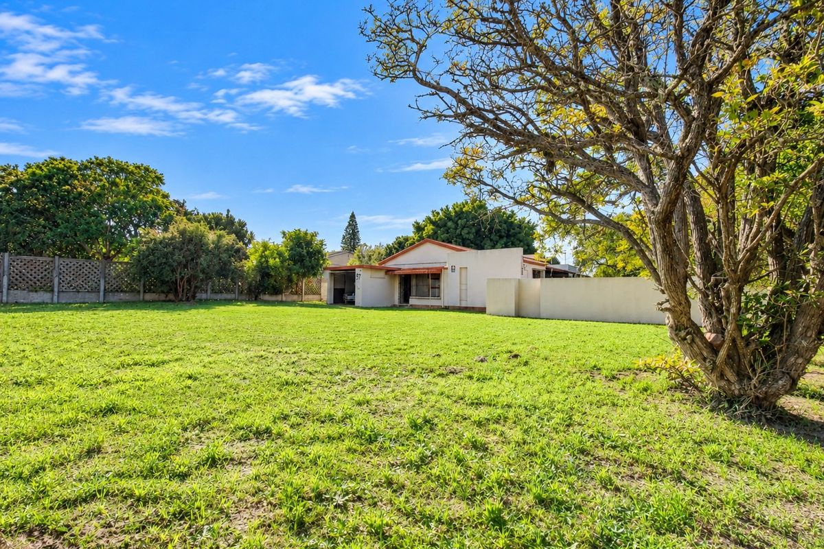 A spacious rear garden featuring a large lawn area, mature tree, and boundary walling, providing a private outdoor space for the property.