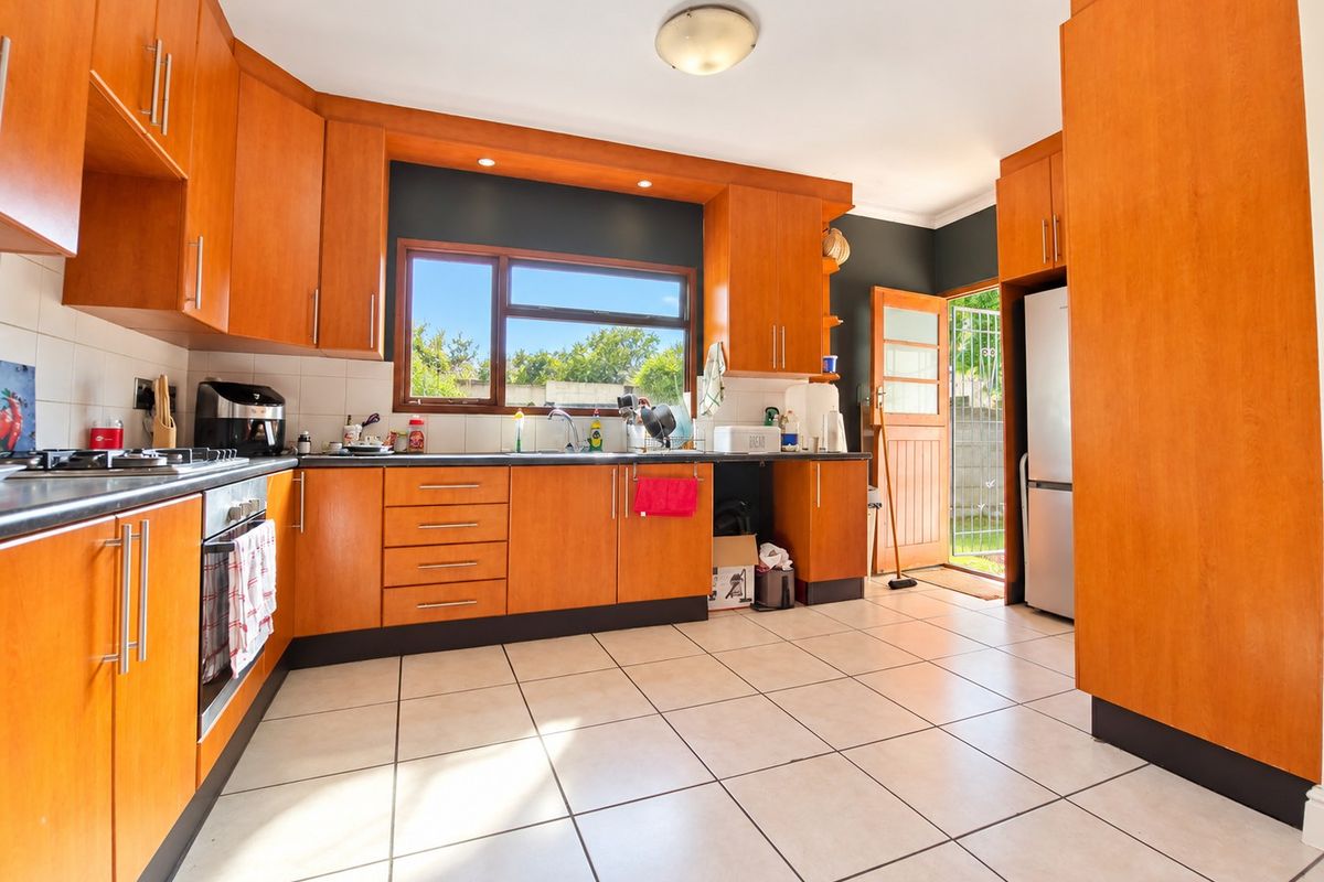 A functional kitchen featuring warm-toned wooden cabinetry, tiled flooring, and direct access to the exterior through a timber door.