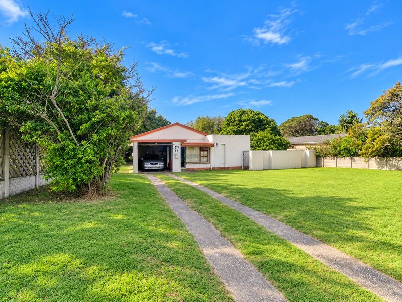 Front view of a single-story house featuring a concrete driveway, attached garage, and a spacious front lawn with established boundary walls.