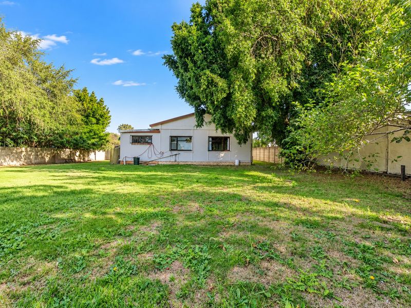 A spacious rear garden featuring a large lawn, mature trees, and a perimeter wall, providing a private outdoor area behind the house.