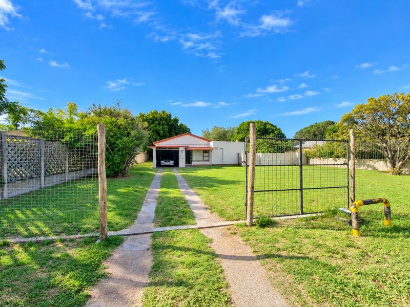 Front view of a single-story house featuring a long concrete driveway, wire mesh perimeter fencing, and an attached garage.