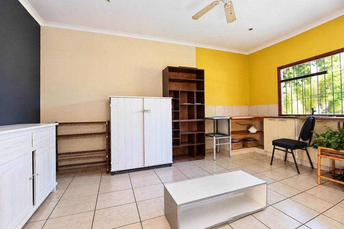 A living area featuring tiled flooring, a ceiling fan, and security bars on the window, offering a functional space with potential for modernization.