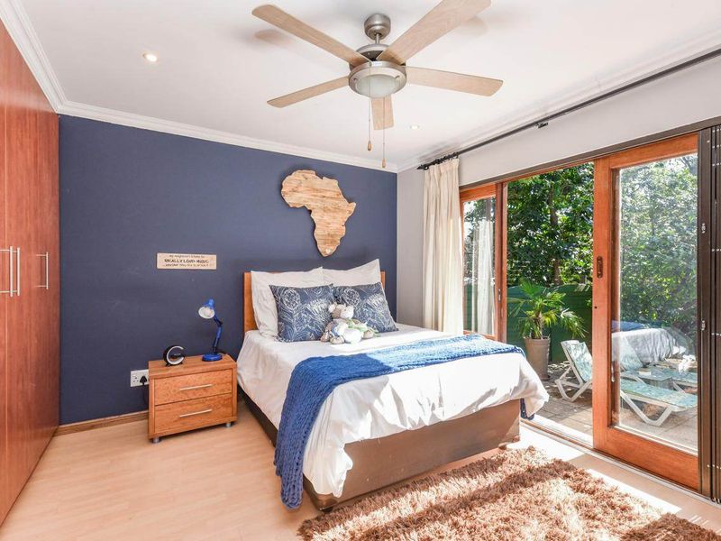 A well-lit bedroom featuring built-in cupboards, a ceiling fan, and sliding glass doors that provide direct access to an outdoor patio area.