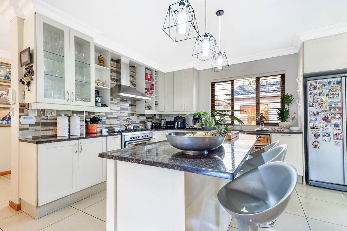 Modern kitchen featuring granite countertops, a central island, gas stove with extractor, and ample built-in cabinetry with glass-front display units.